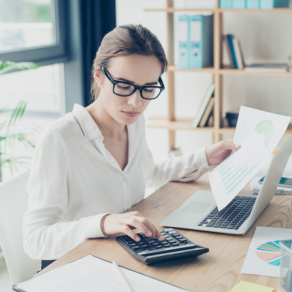Eine Frau mit Brille sitzt am Schreibtisch und berechnet ihre Arbeitskraftabsicherung