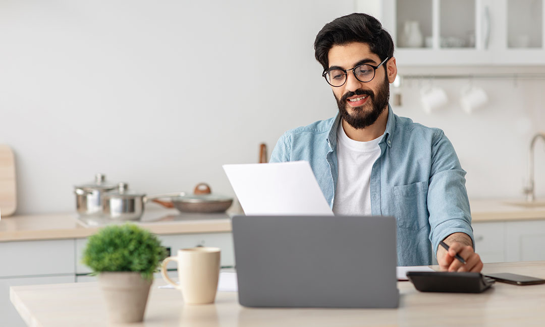 Mann mit Laptop schaut auf ein Blatt Papier