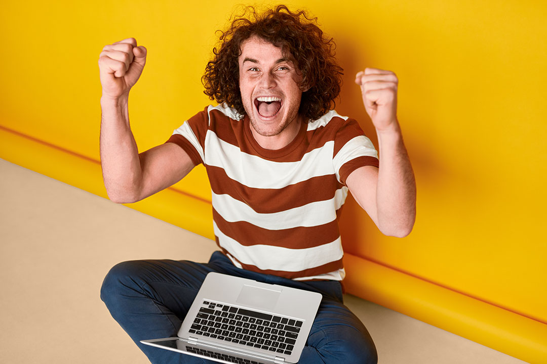 Mann mit Laptop lacht in die Kamera