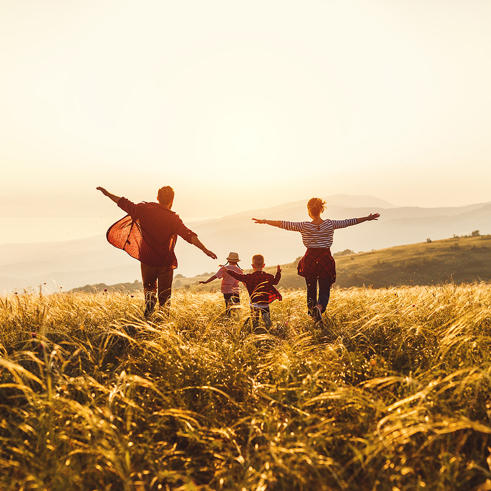 Eine Familie springt fröhlich im Abendlicht über ein Feld am Meer